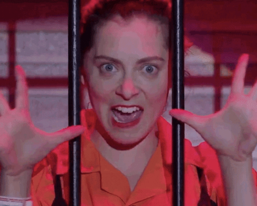 A woman behind bars with her hands up, like she&#x27;s singing a song and doing jazz hands