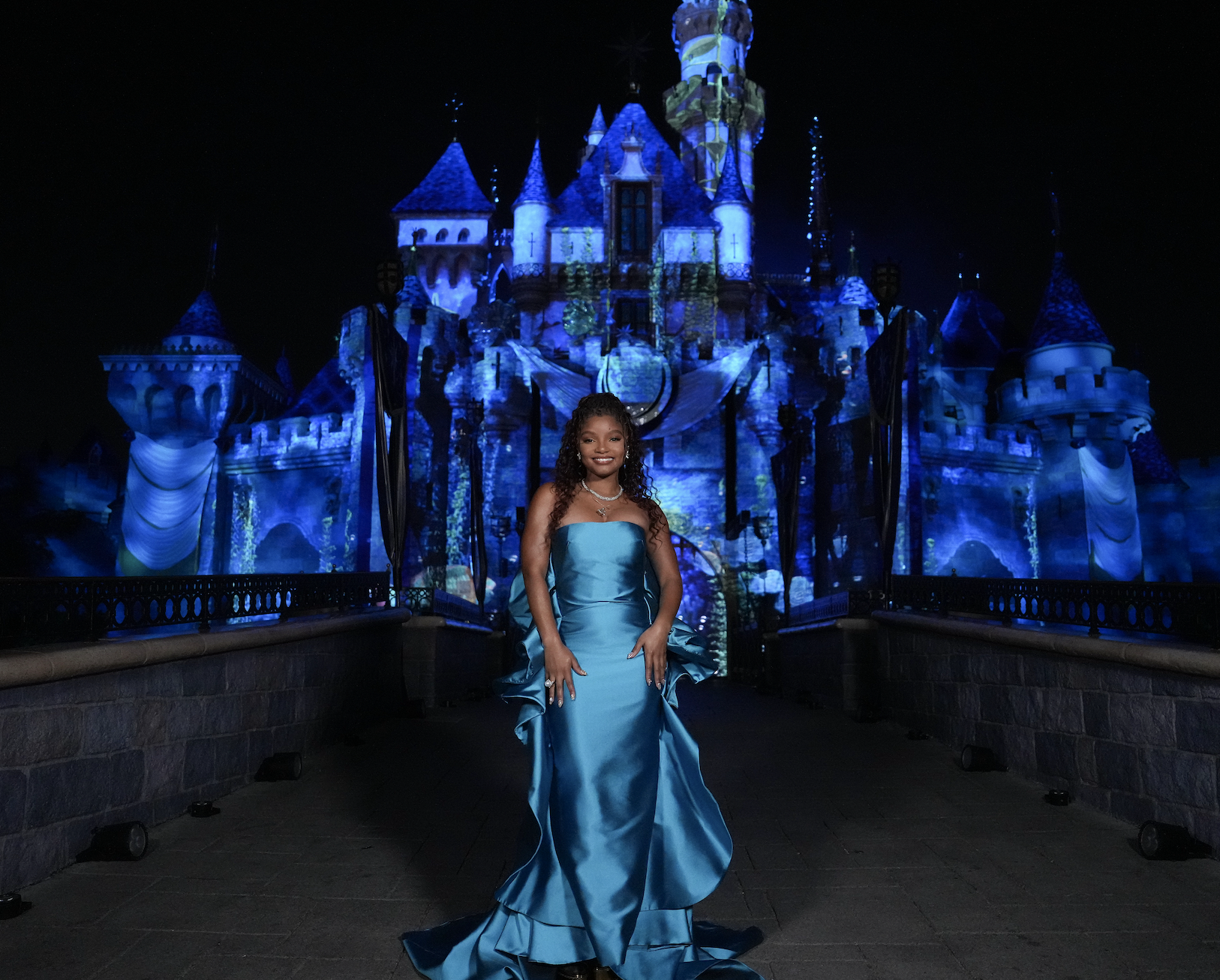 Halle standing in front of the castle in a long shiny strapless dress