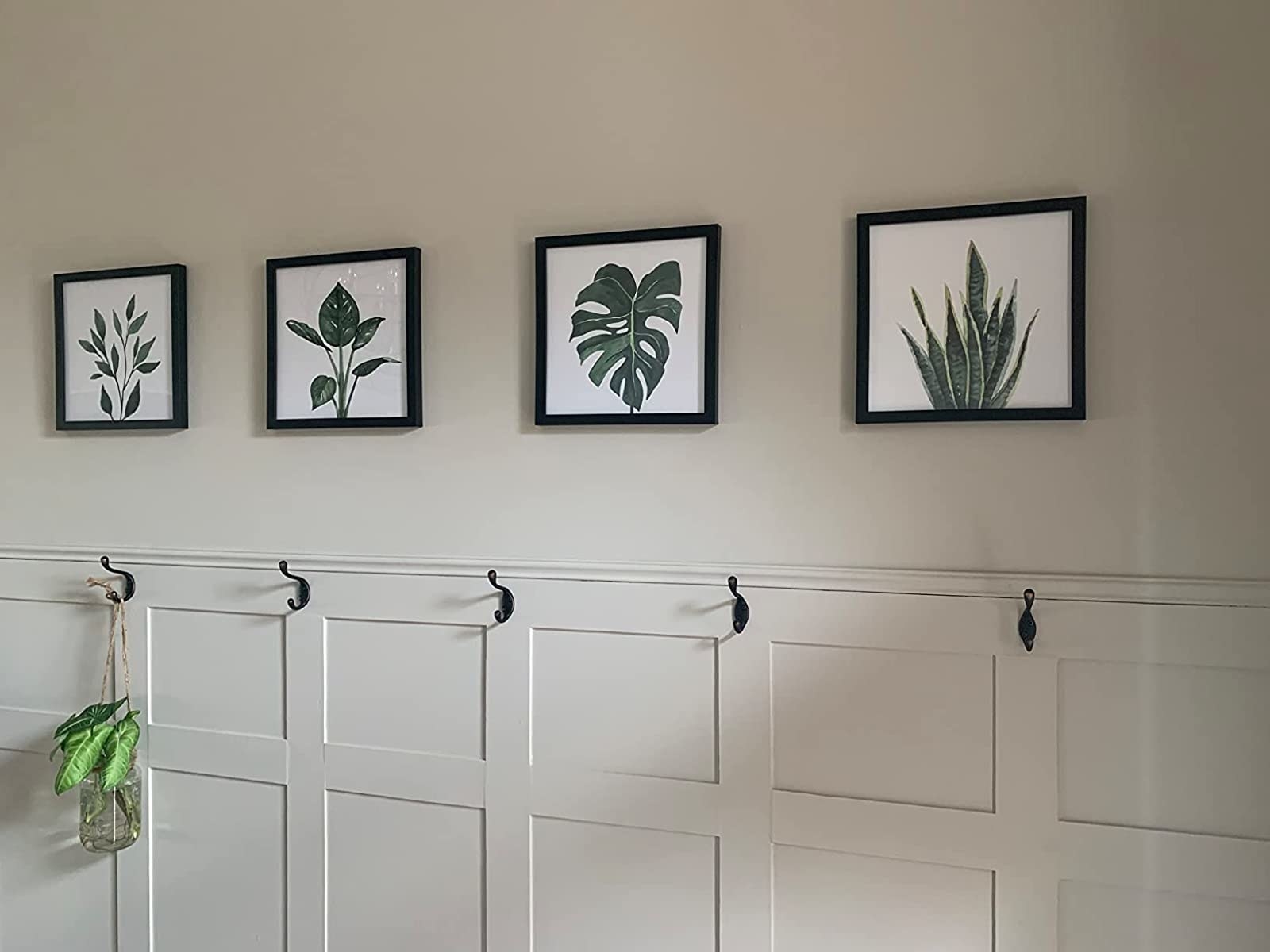 The prints displayed on a white wall above several coat hooks