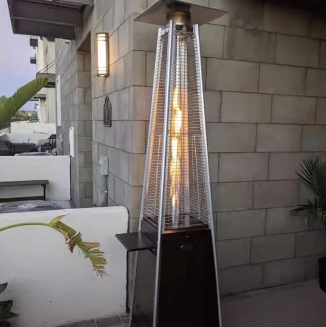 Outdoor patio heater with flame inside glass tube next to furniture