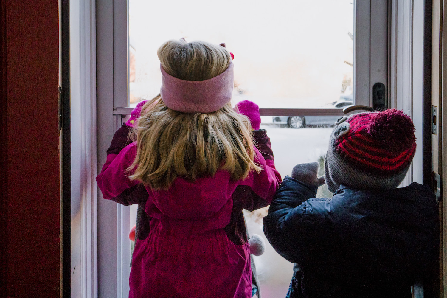 kids bundled up looking at the snow outside