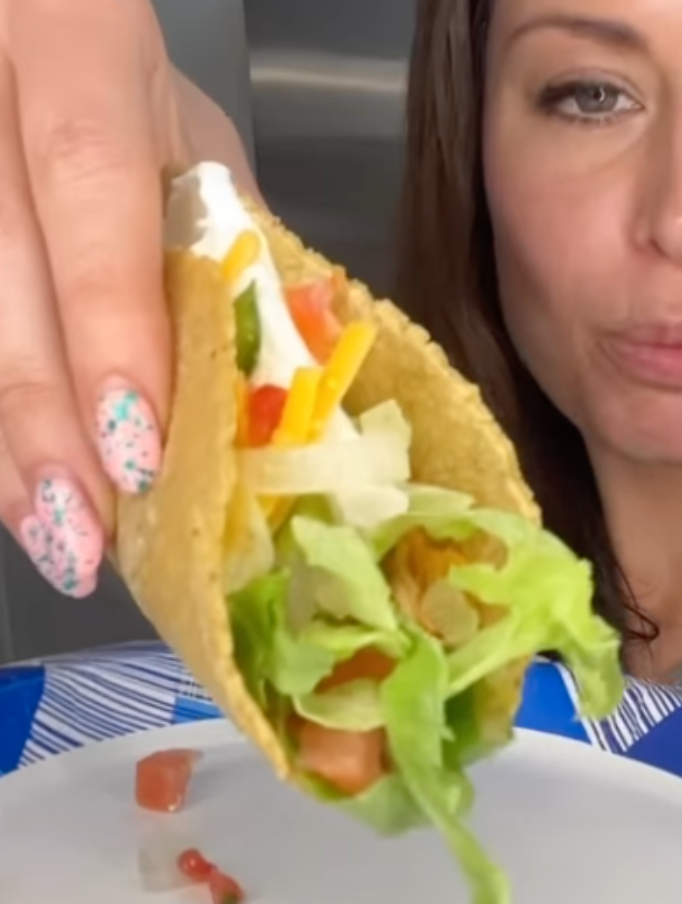 Krista holding up a taco filled with chicken goop, lettuce, and tomato