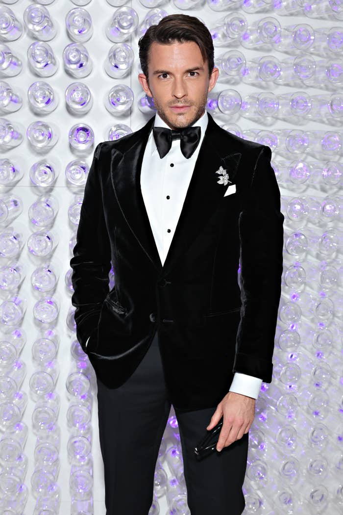 jonathan bailey poses on red carpet in a tuxedo with a velvet jacket