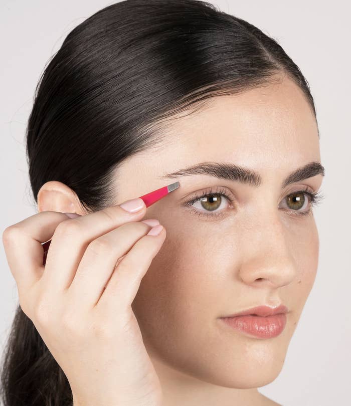 Model using pink Tweezerman tweezers to remove hair on their eyebrows