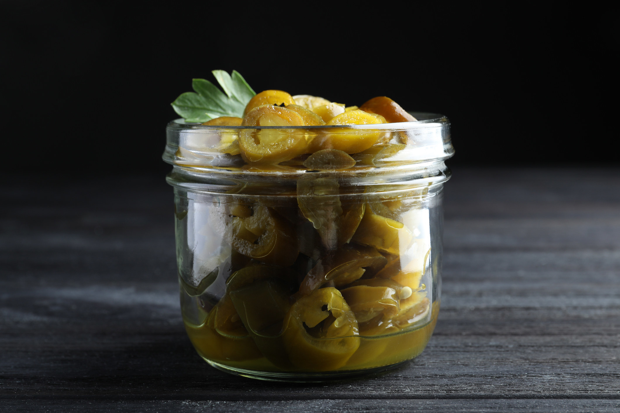 Glass jar with slices of pickled green jalapeño peppers.