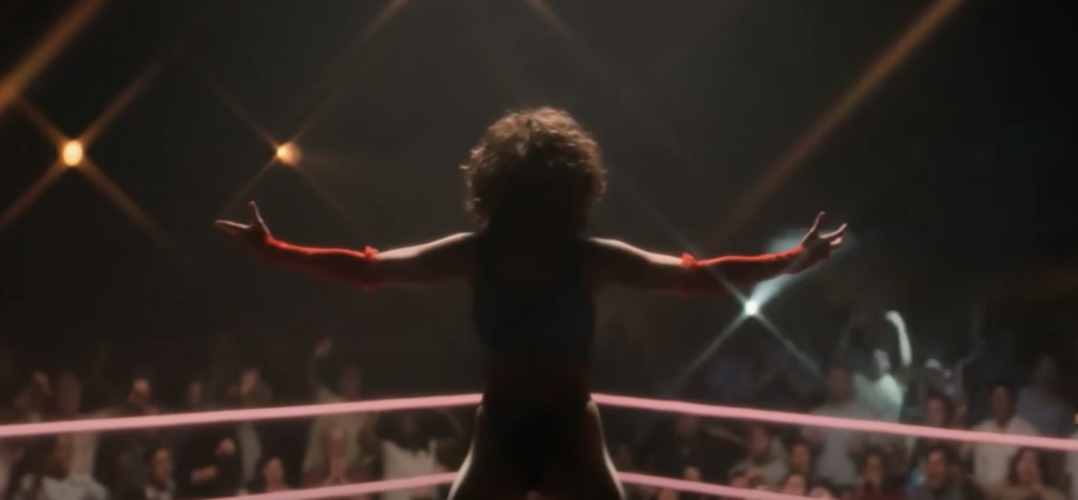 A female wrestler stands in the ring with her arms spread wide toward the crowd in a scene from &#x27;GLOW&#x27; on Netflix