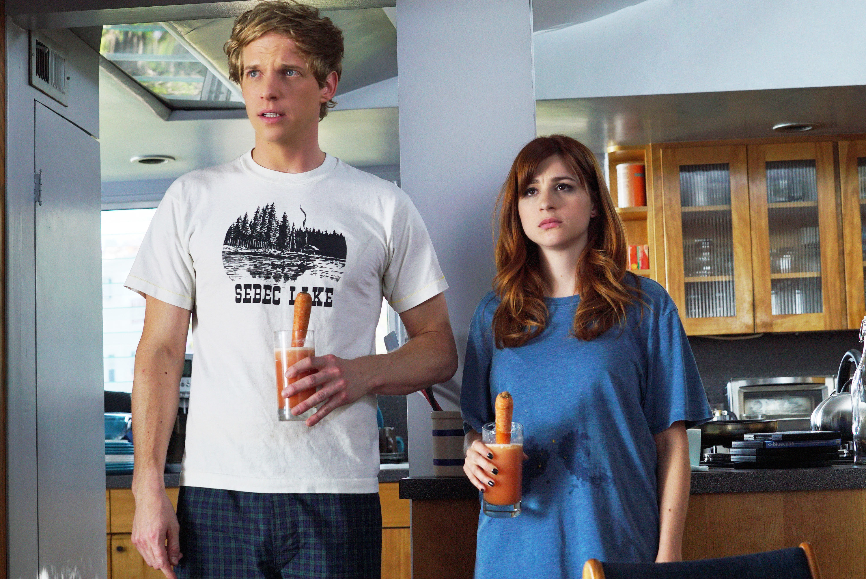 a couple standing in the middle of the kitchen holding carrot juice with large carrots in them