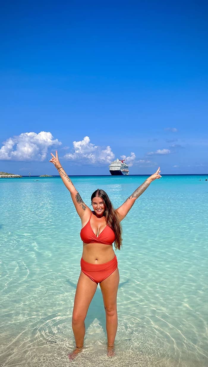 Reviewer standing in turquoise waters in orange bikini with hands above head