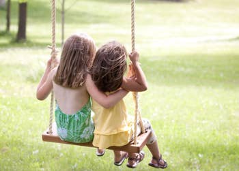 Two small girls sit on a tree swing