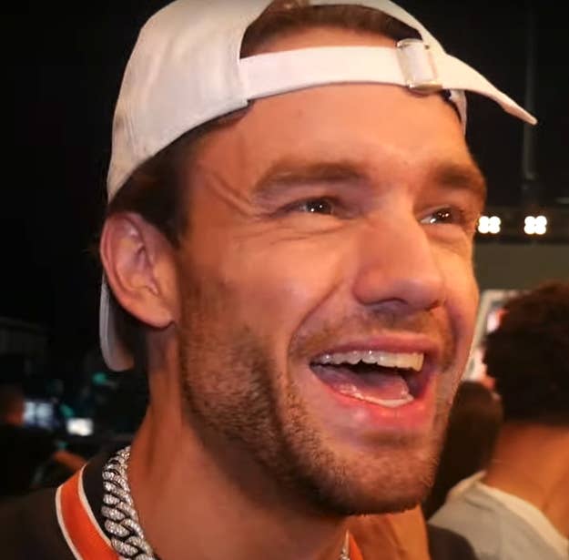 A closeup of Liam Payne smiling. He's wearing a cap backwards and what looks to be a diamond chain