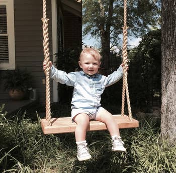 A toddler sits on a tree swing