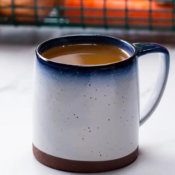 A ceramic mug filled with a hot beverage is placed on a table. The mug has a speckled white and navy blue gradient design