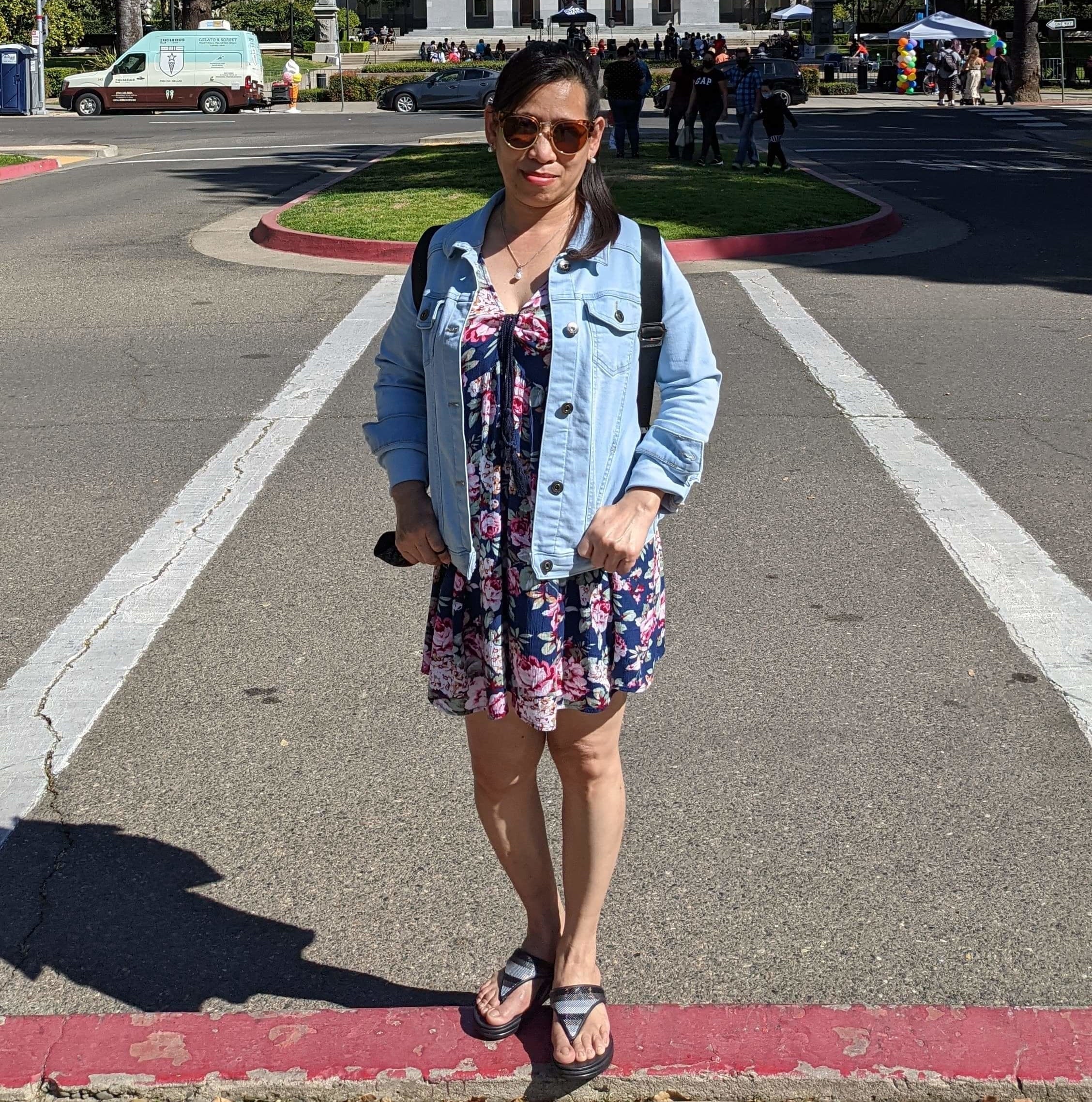 Reviewer wearing light blue jacket over dress while standing in front of legislative building