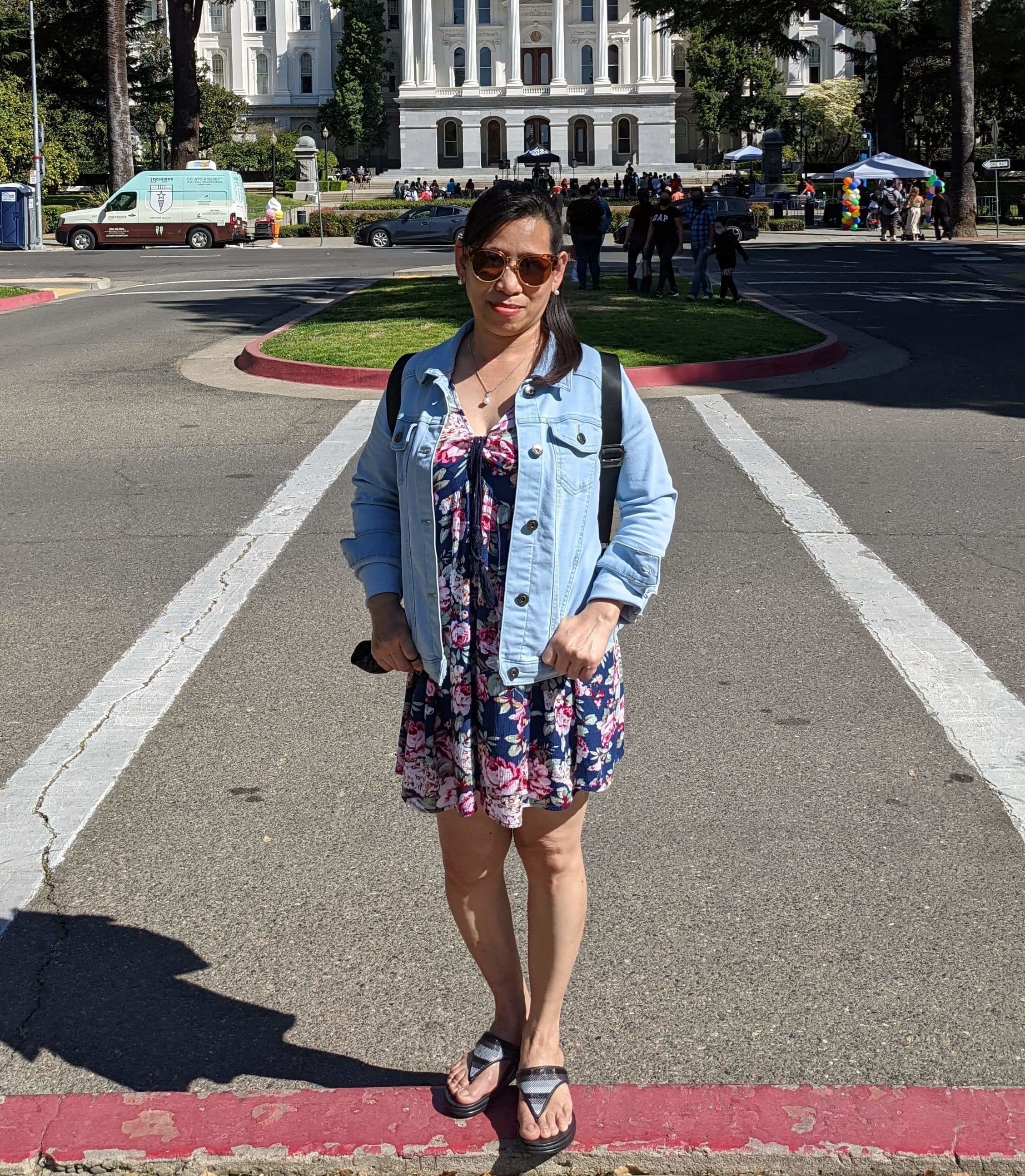 Reviewer wearing light blue jacket over dress while standing in front of legislative building