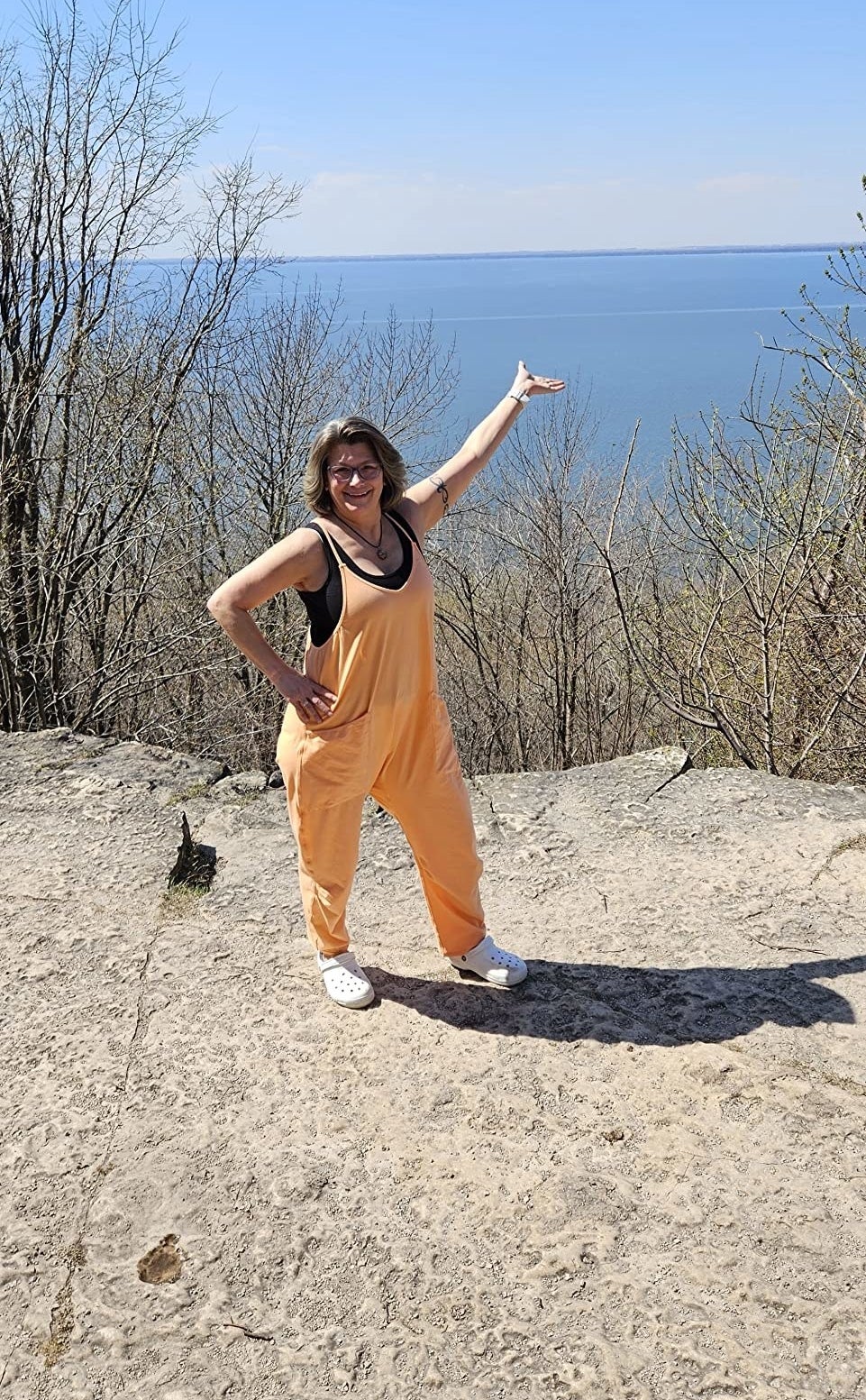 Reviewer posing on mountain in front of water in orange jumper