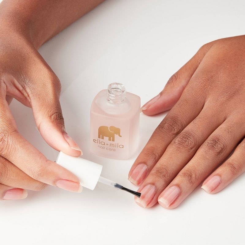 A person applying nail strengthener to their nails