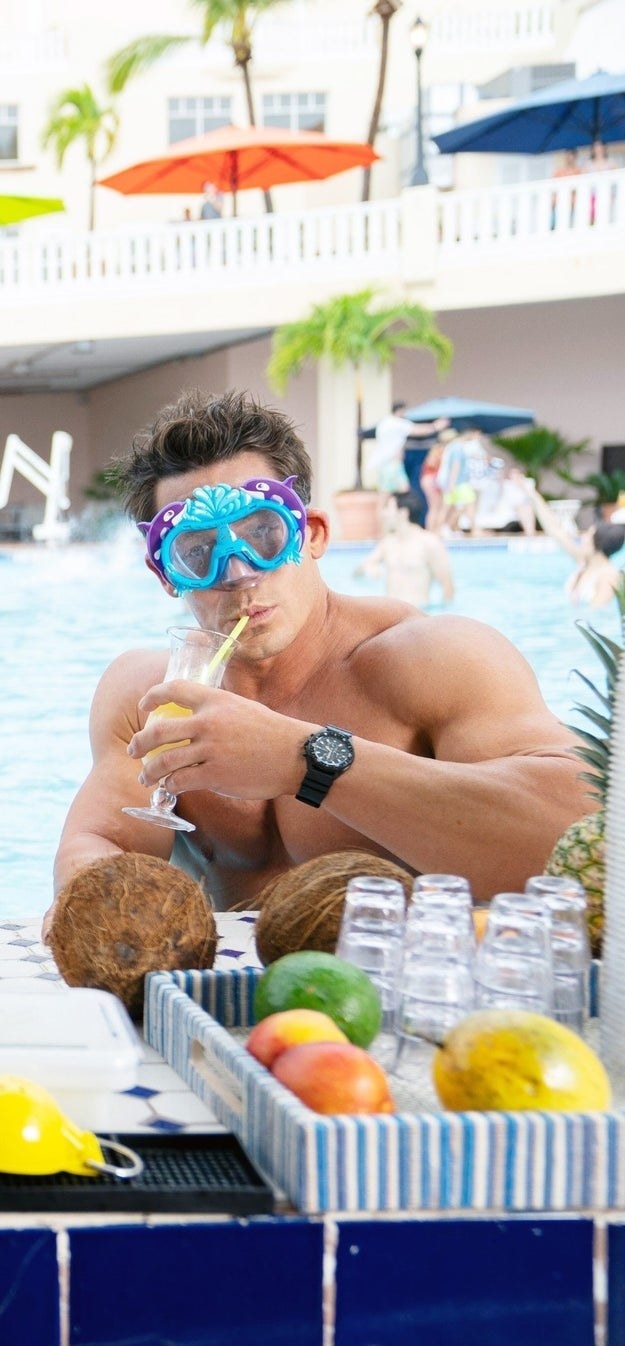Closeup of John Cena sitting in a pool and sipping a drink while wearing a toy-ish looking pair of goggles