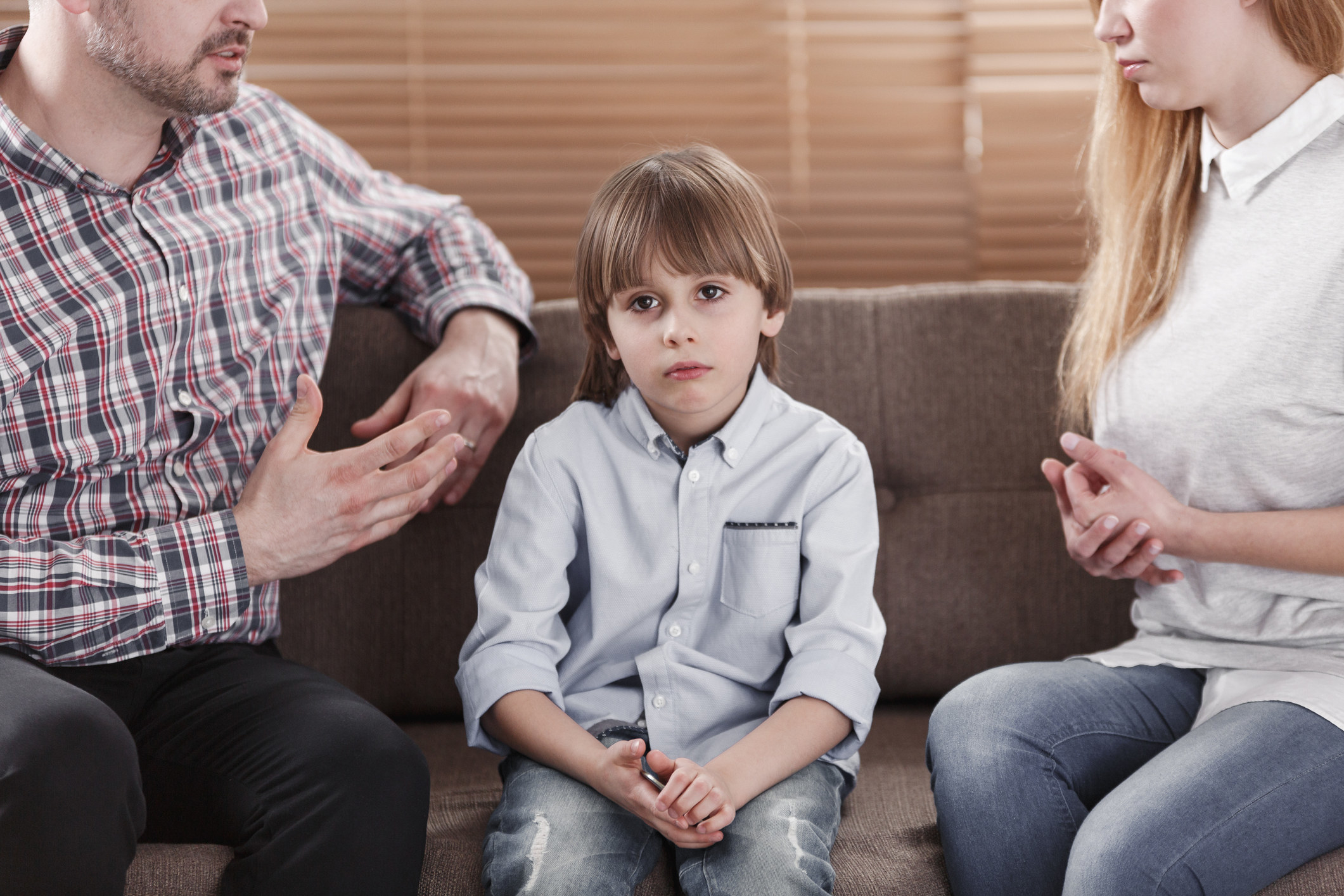 Sad young boy sitting in-between fighting parents
