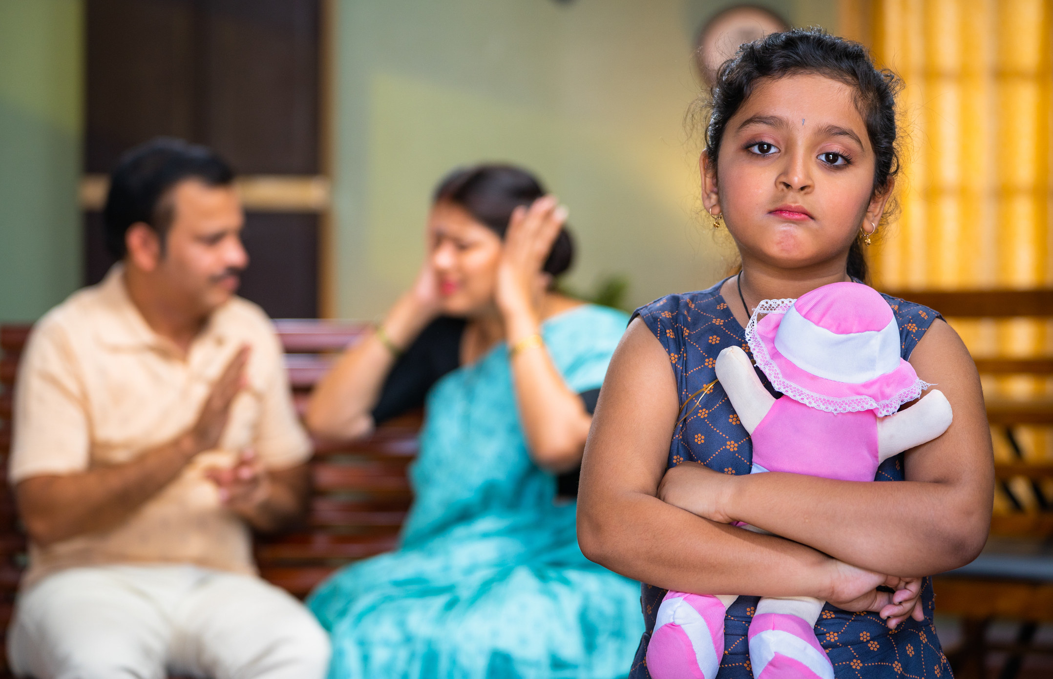 Upset young girl with parents fighting in the background