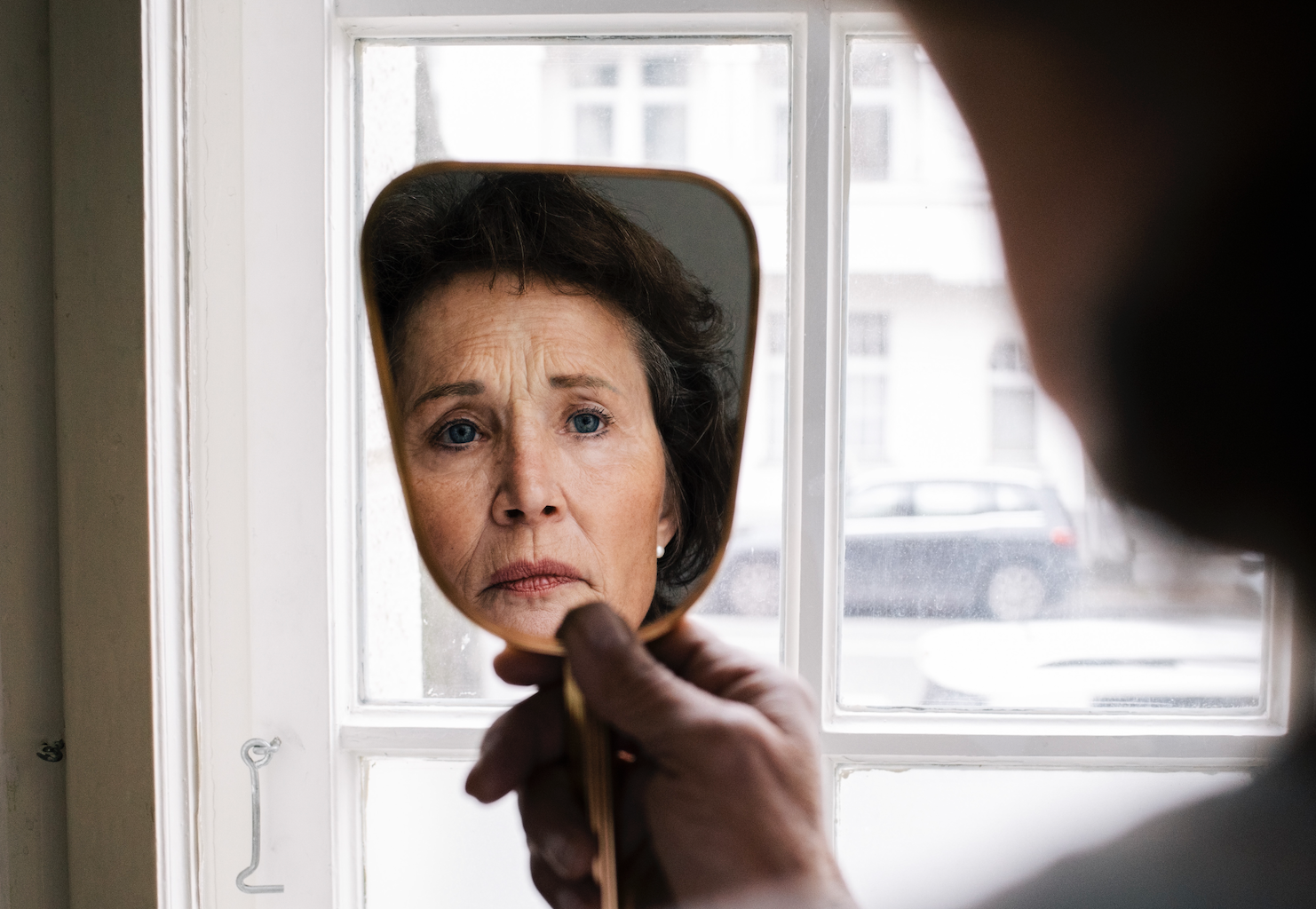 Old woman frowning at her reflection in a hand-held mirror