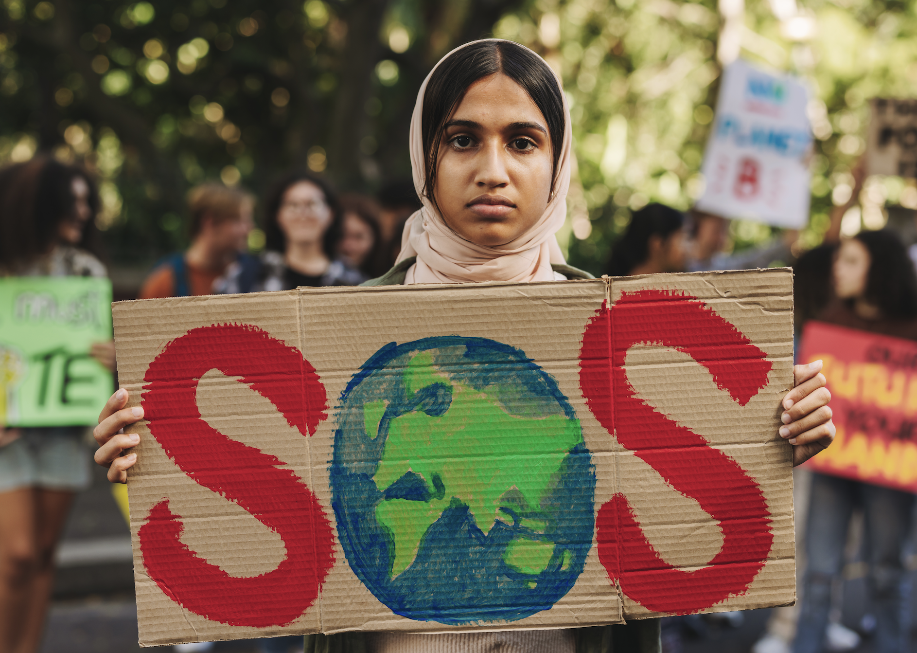 Young woman wearing a hijab while holding a protest sign that reads &quot;SOS&quot;