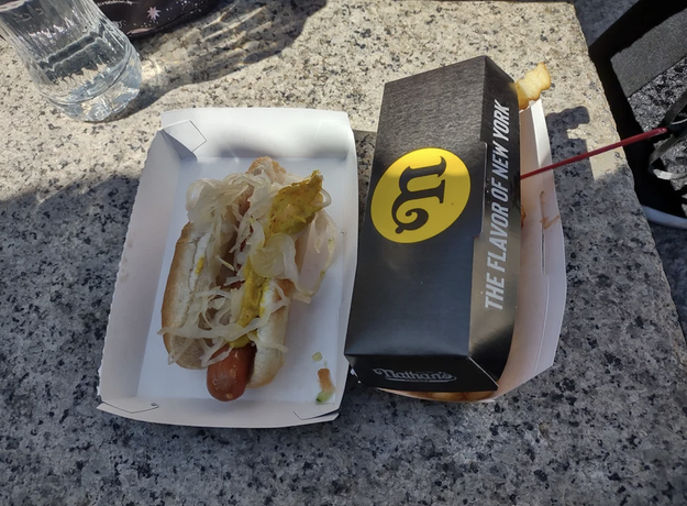 hot dog with onions and mustard next to a box with text that says &quot;Nathan&#x27;s: The flavor of New York&quot;