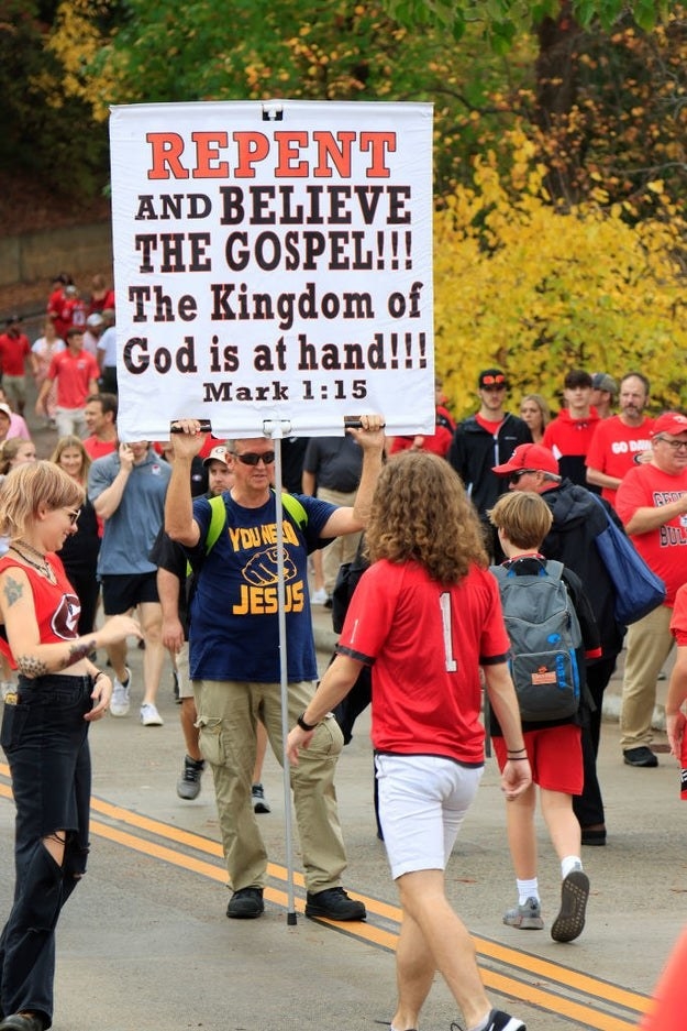 男人站在一群人举着牌子说“悔改,相信福音。神的国就在眼前! ! !马克1:15"