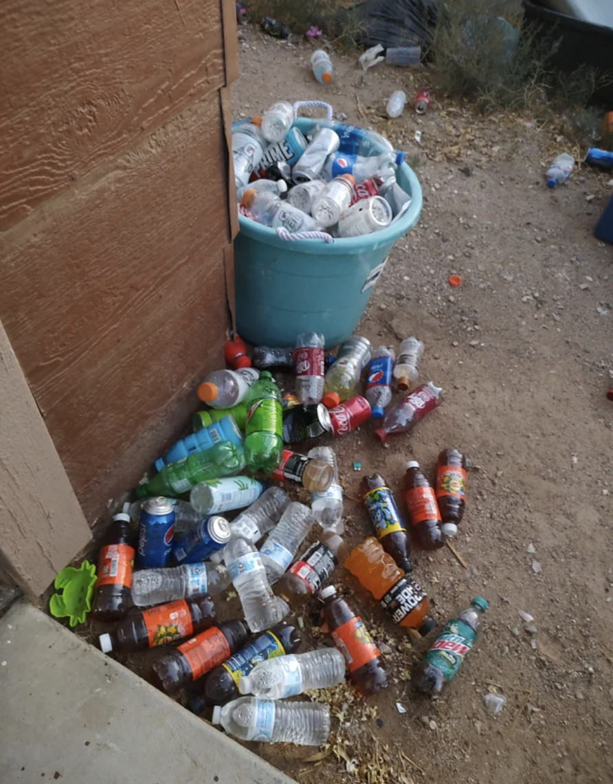 A bin is full of plastic bottles, so a huge stack of other bottles have been thrown on the ground next to the bin