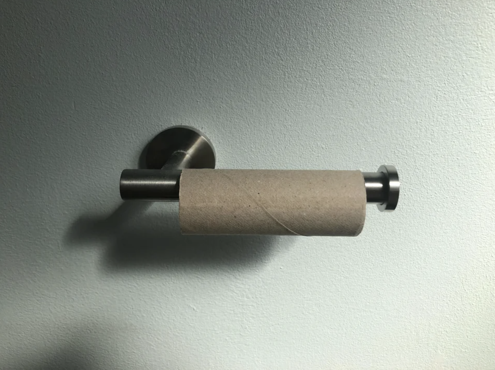 An empty roll of toilet paper has been left on the holder, and the picture has been taken from the angle of someone sitting on the toilet