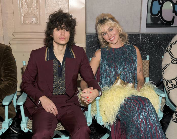 Maxx Morando and Miley Cyrus holding hands while sitting front row for Gucci Love Parade
