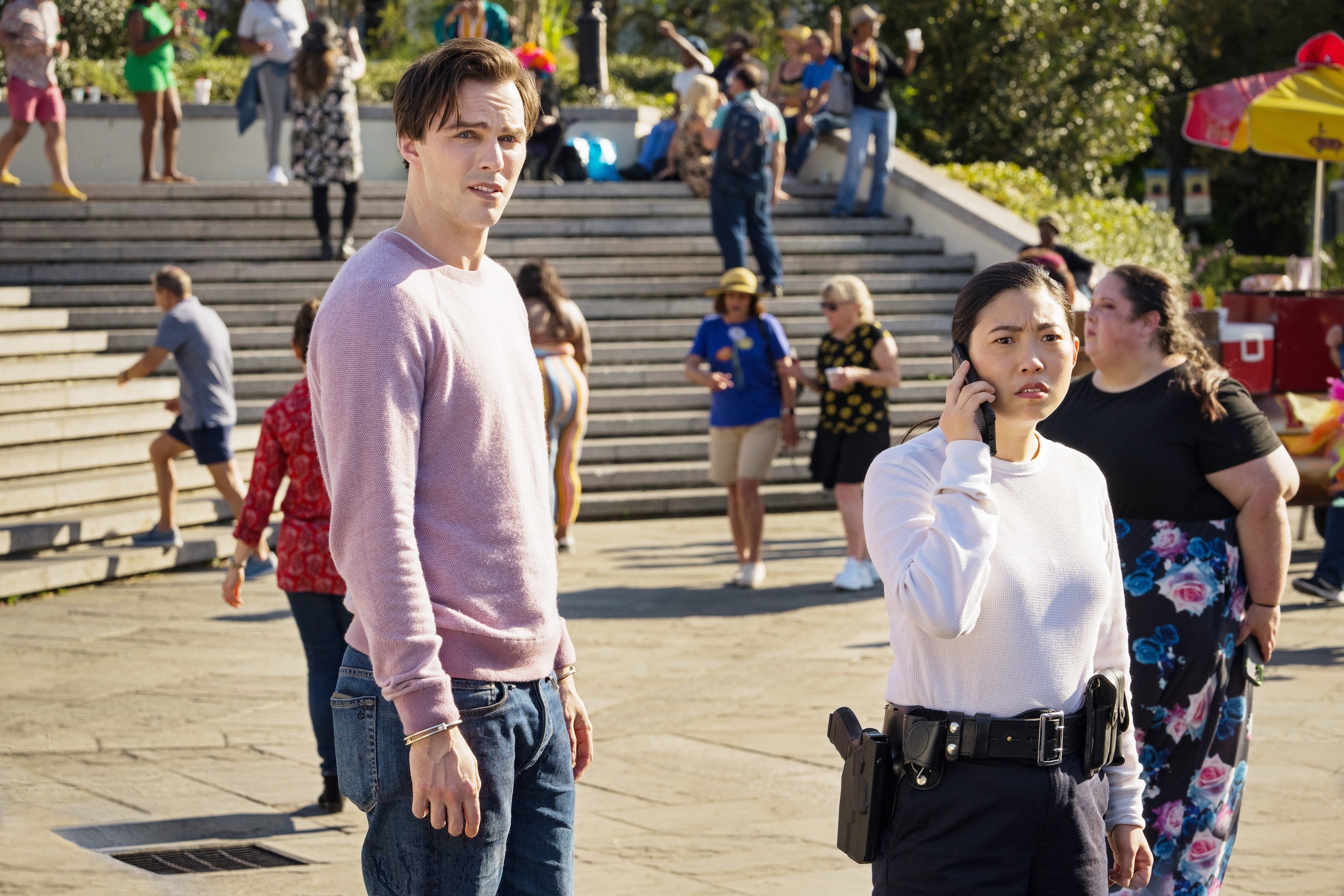 Nicholas Hoult and Awkwafina take a call in a crowded outdoor plaza in Renfield