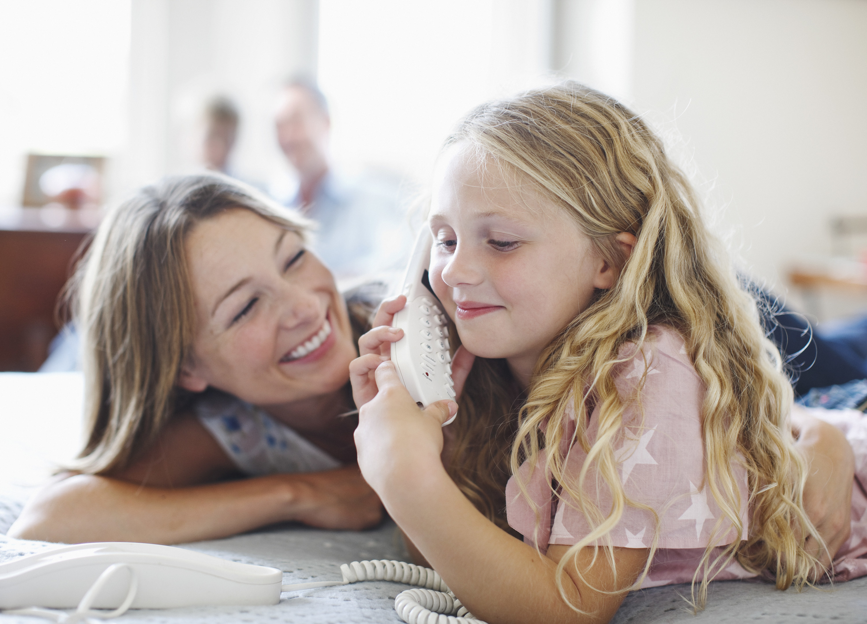 A woman smiles as her daughter talks on a landline telephone