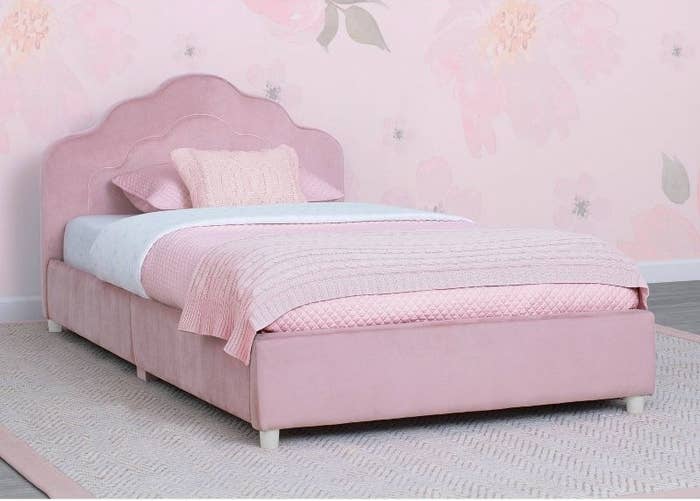 a pink upholstered bed in a bedroom with pink floral wallpaper and a pink rug