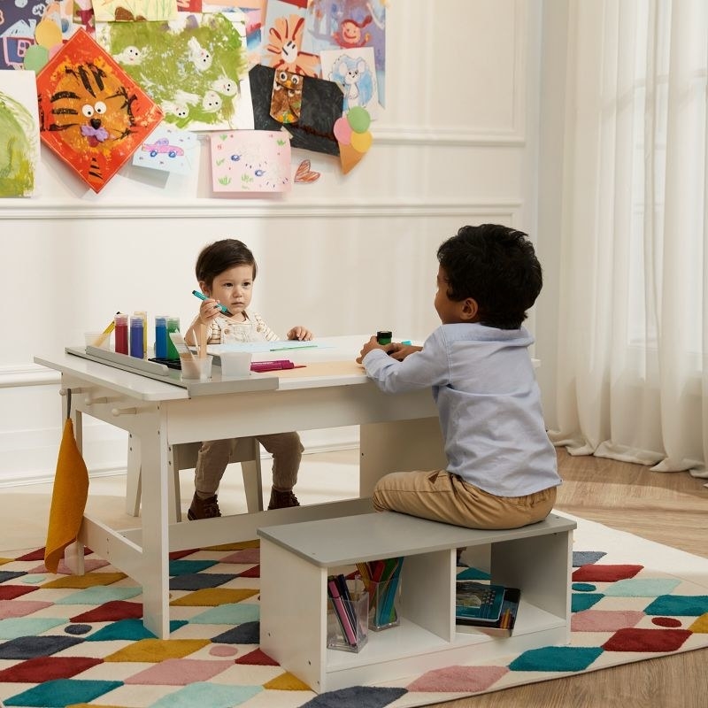two children sitting across from each other coloring at an art table on a geometric rug