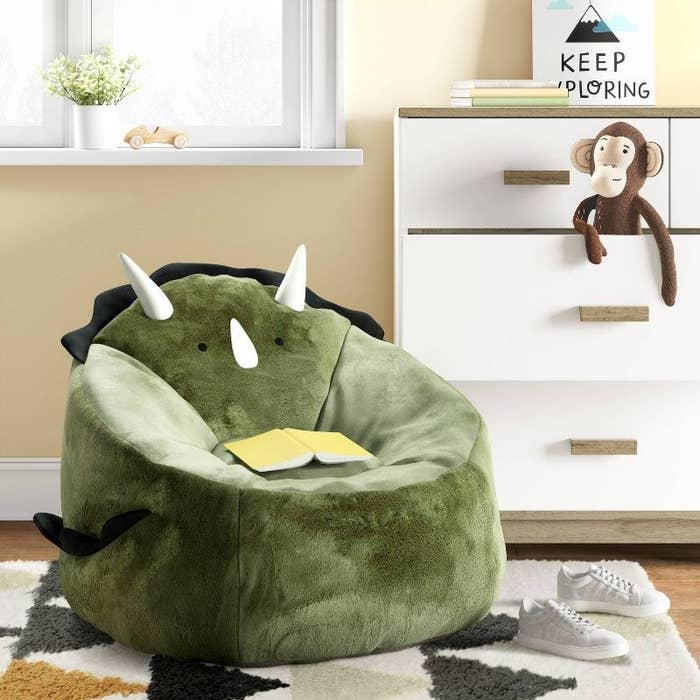 a dinosaur bean bag chair on top of a geometric rug next to a chest of drawers