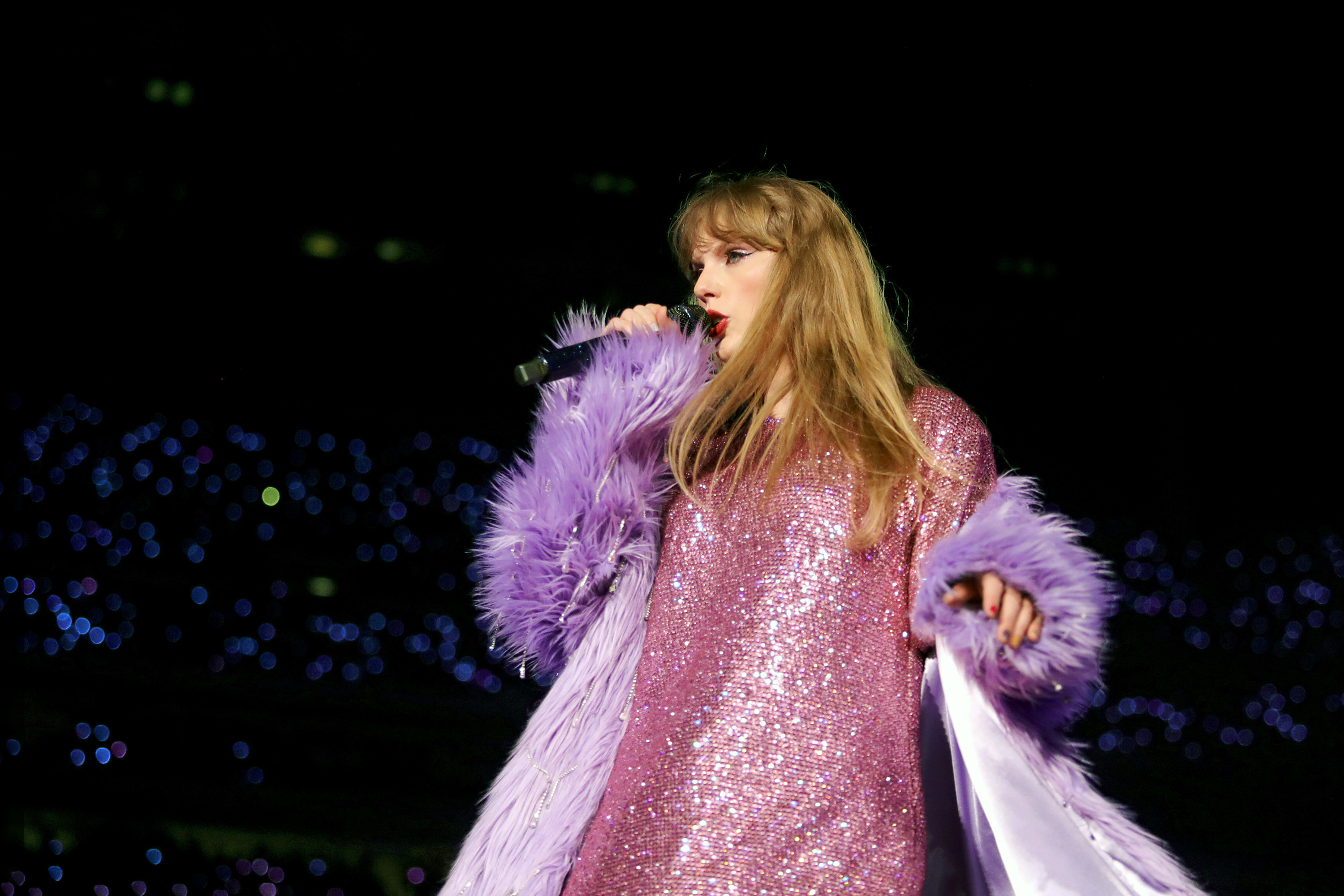 Taylor Swift wearing a pink t-shirt dress and purple shaggy jacket