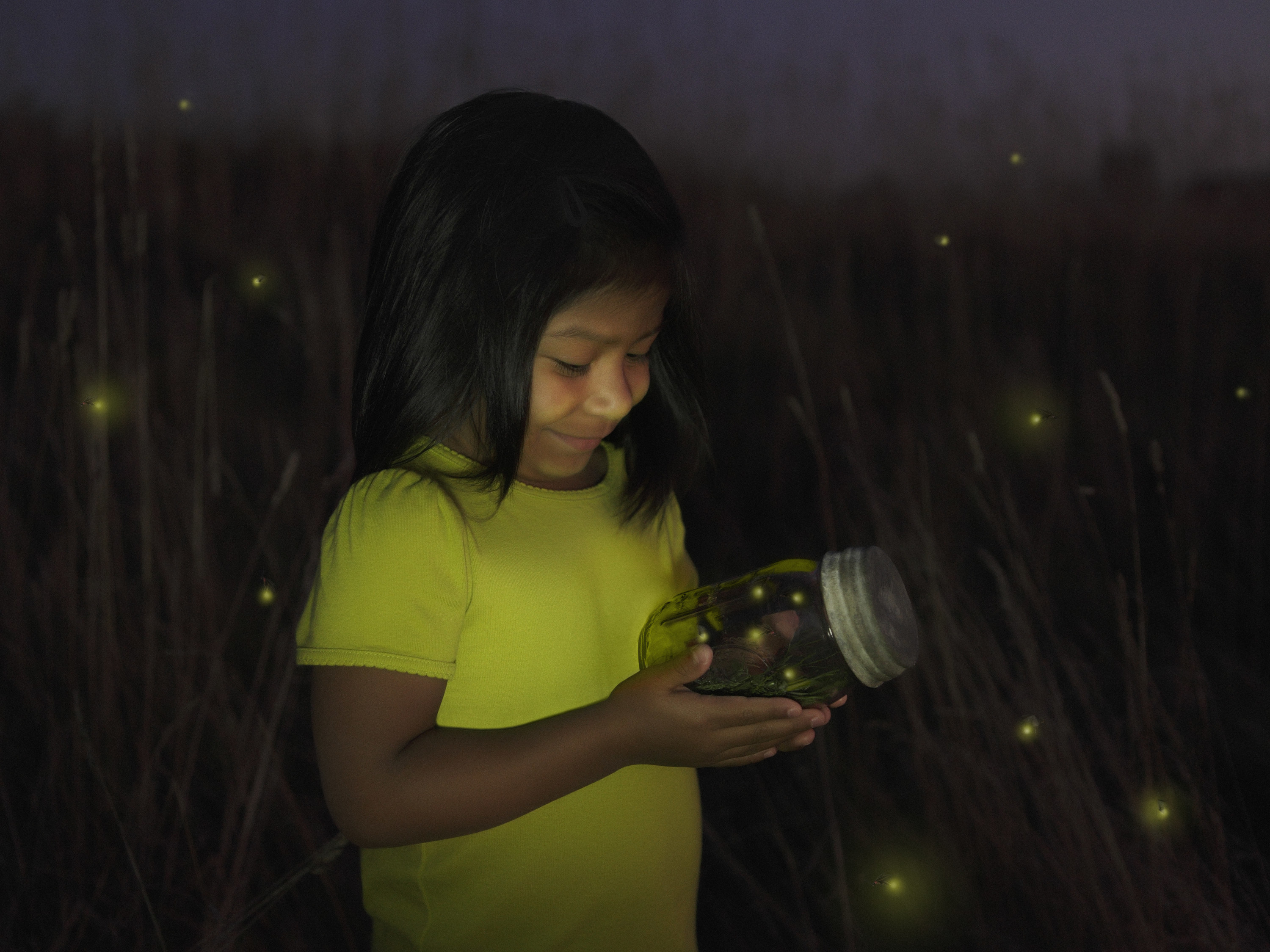 A young girl catches fireflies in a jar
