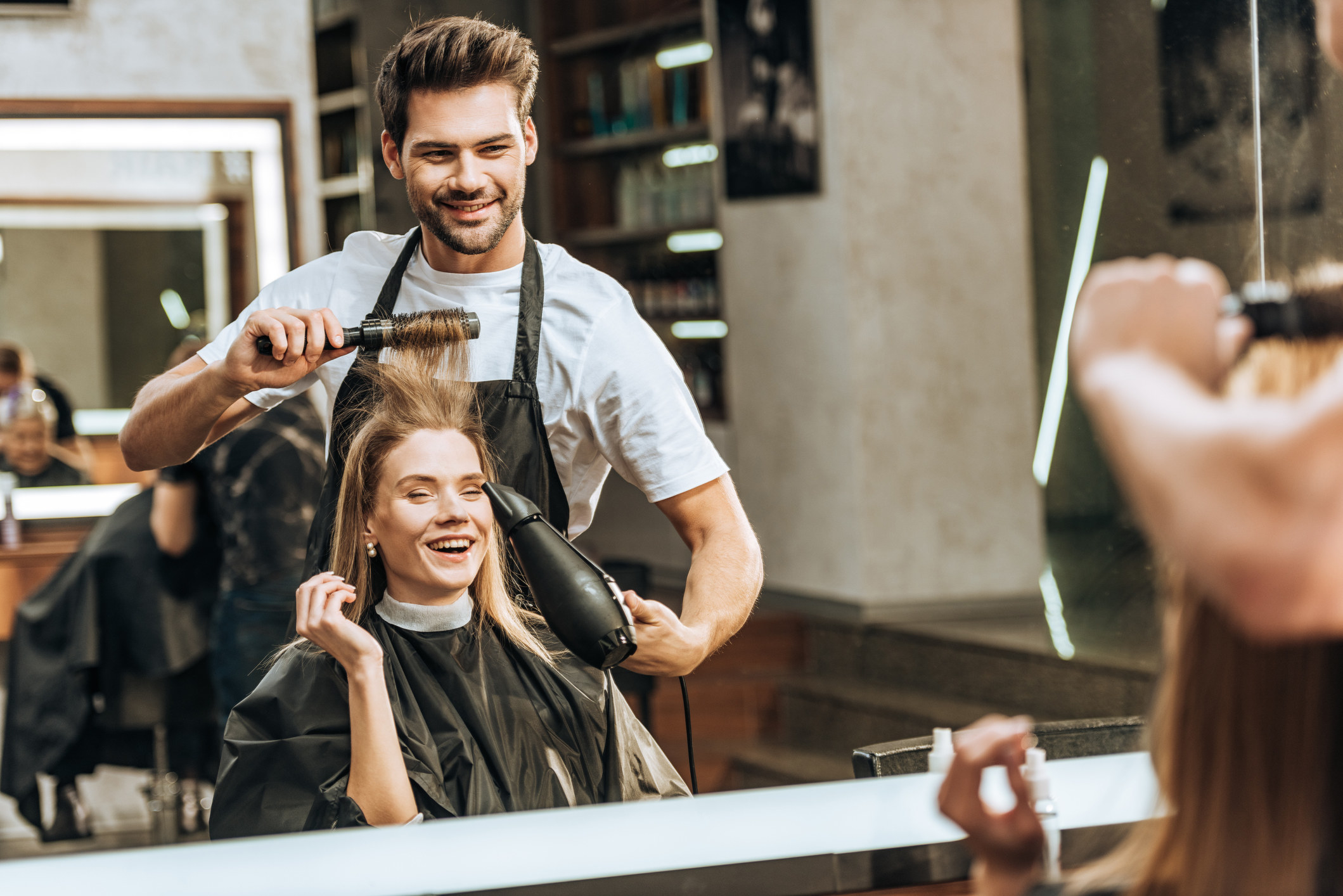 Male hairdresser blow-drying a woman&#x27;s hair