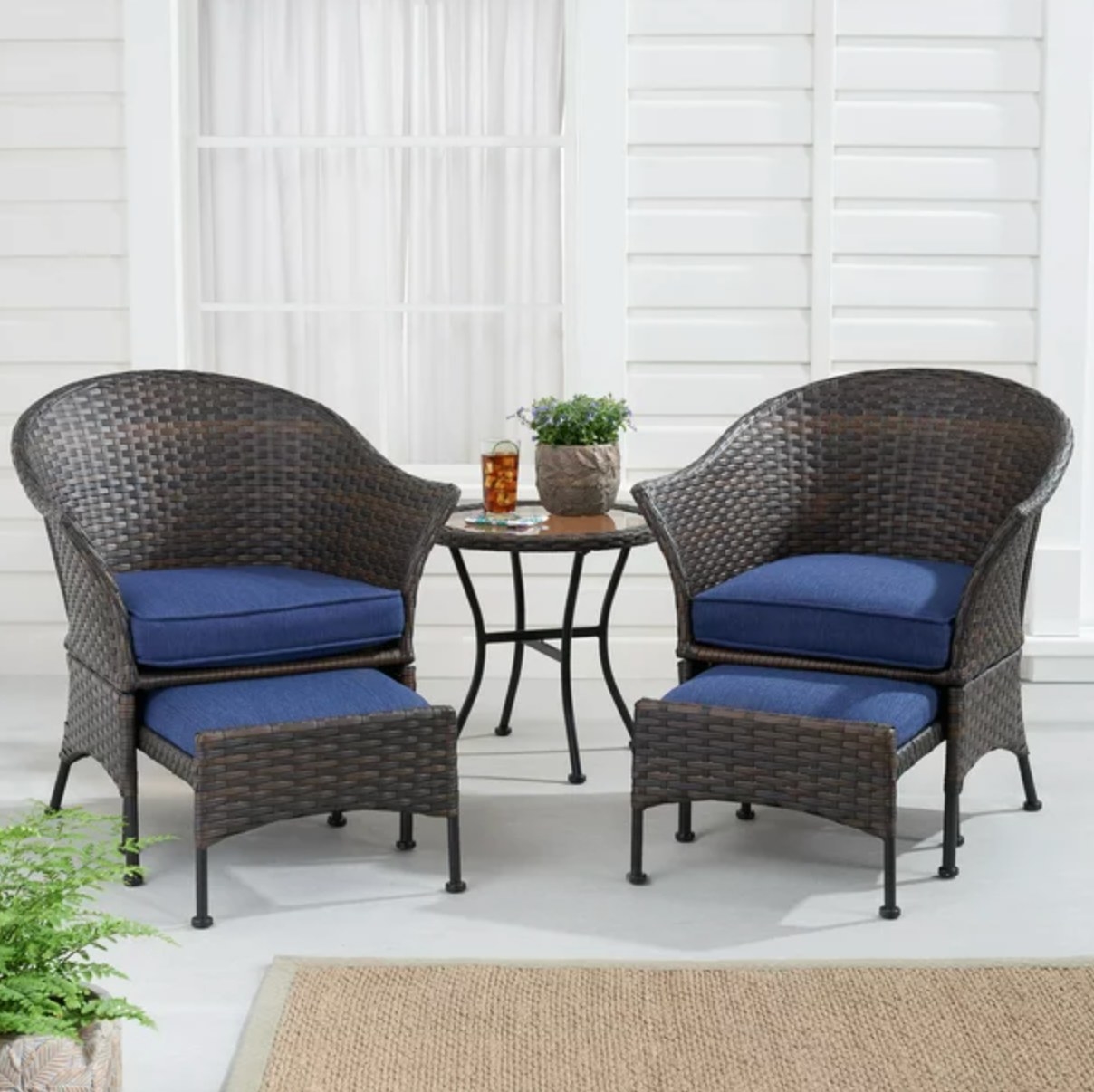 the dark wicker chairs, table, and ottomans with dark blue cushions in a decorated outdoor space