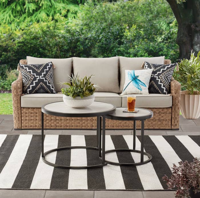 the wicker couch with tan cushions and the round nesting tables in a decorated patio space