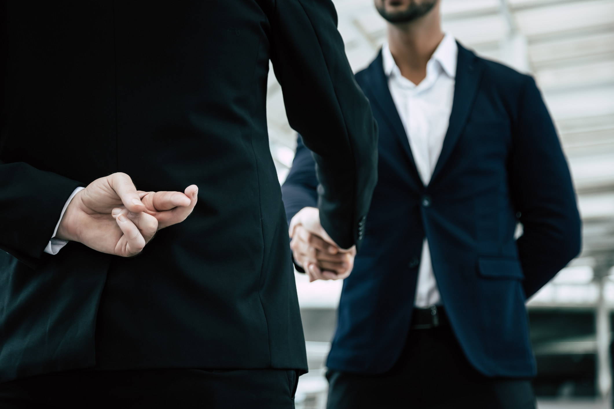 Man crossing fingers behind his back while shaking hands with another man