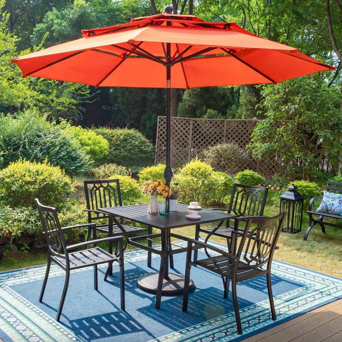 the dark metal table and chairs with a large orange umbrella in a decorated patio space