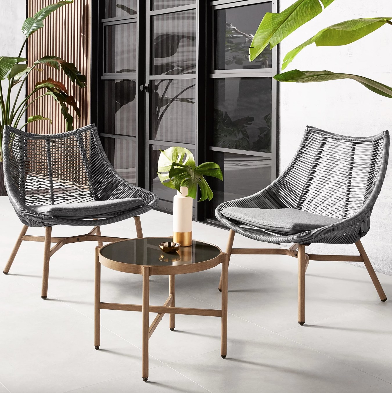 the grey chairs with wooden legs and the glass topped table in a decorated patio space