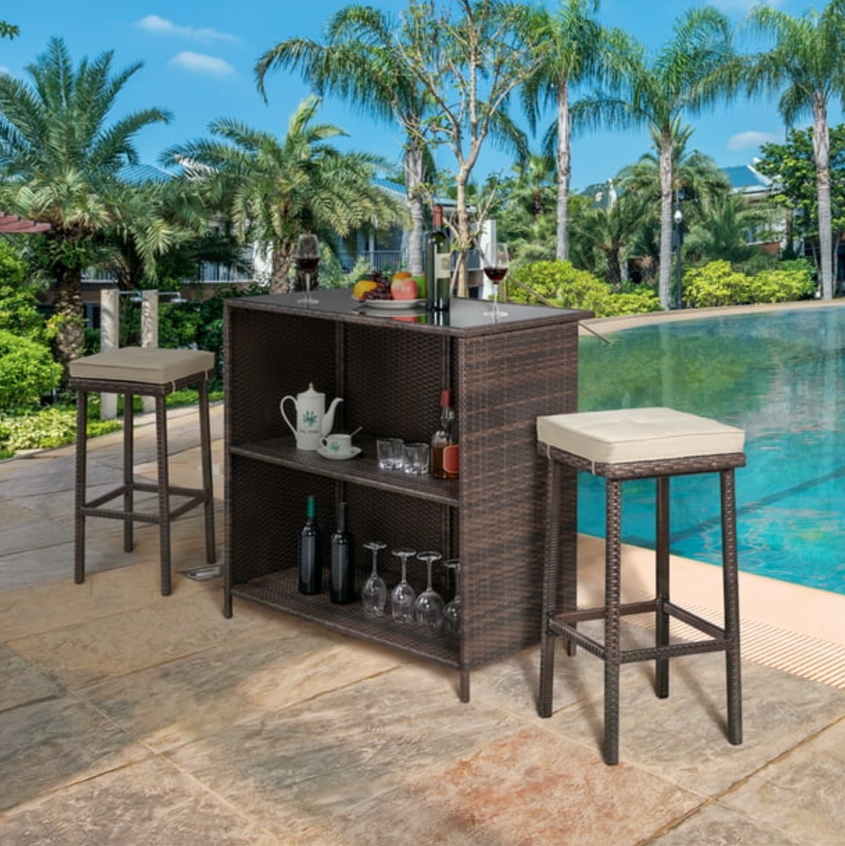 the dark rattan bar table and stools with tan cushions on a decorated pool deck