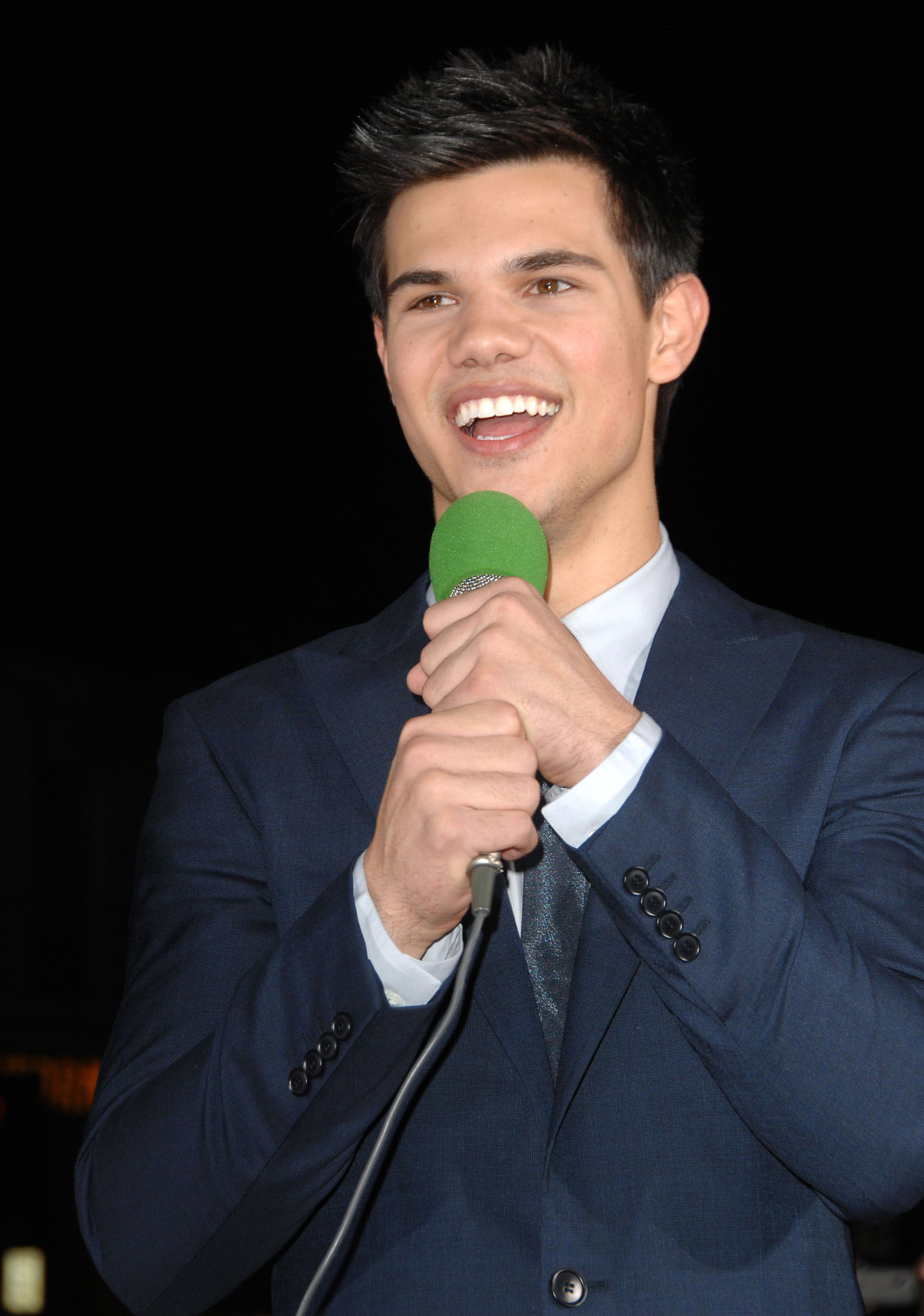 Close-up of Tyler in a suit and tie and holding a microphone