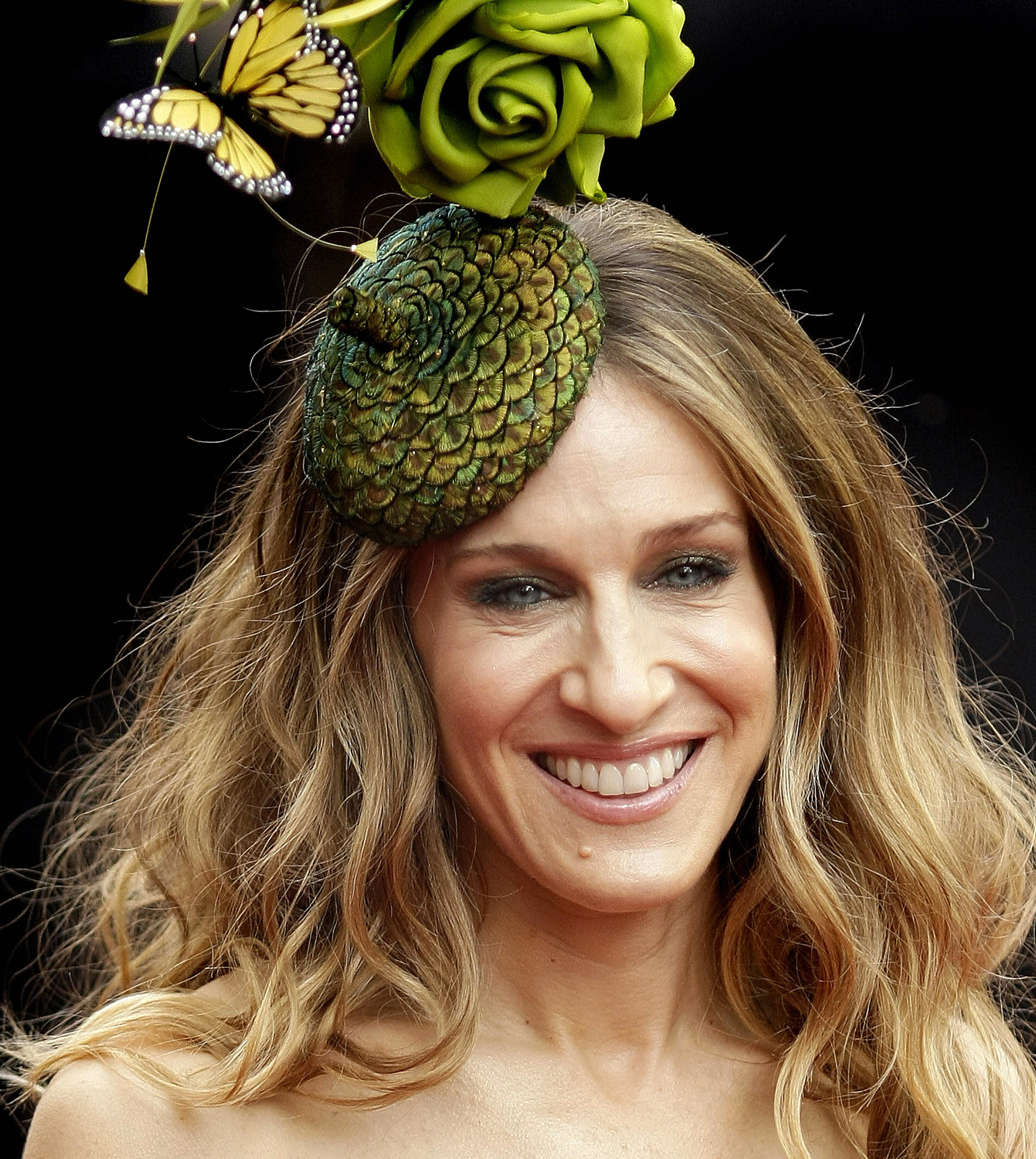 A close-up photo of Sarah Jessica Parker wearing an extravagant green hat, a mole on her chin is very visible