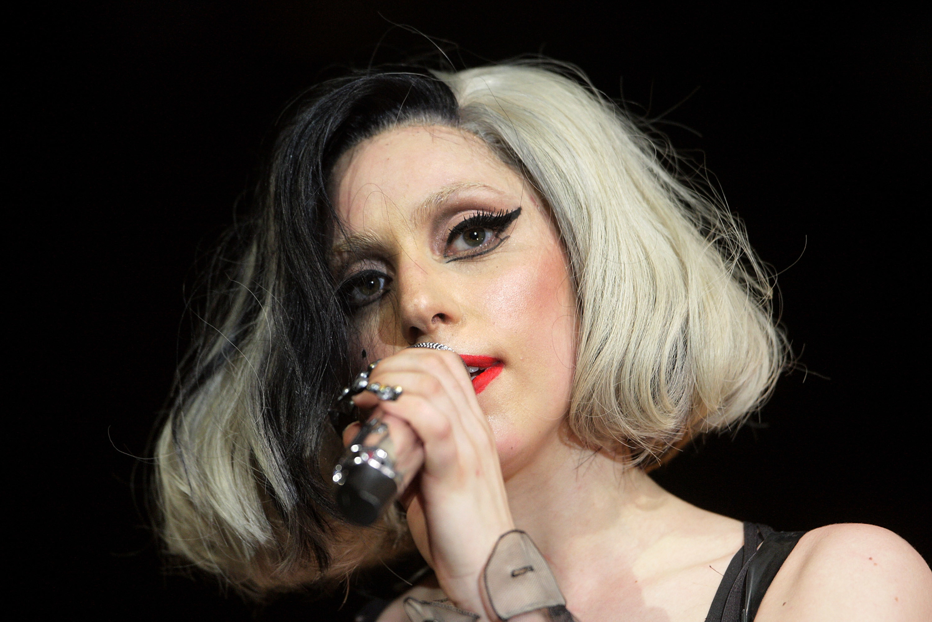 Lady Gaga performs on stage with heavy black eye makeup, her hair is half blonde and half black