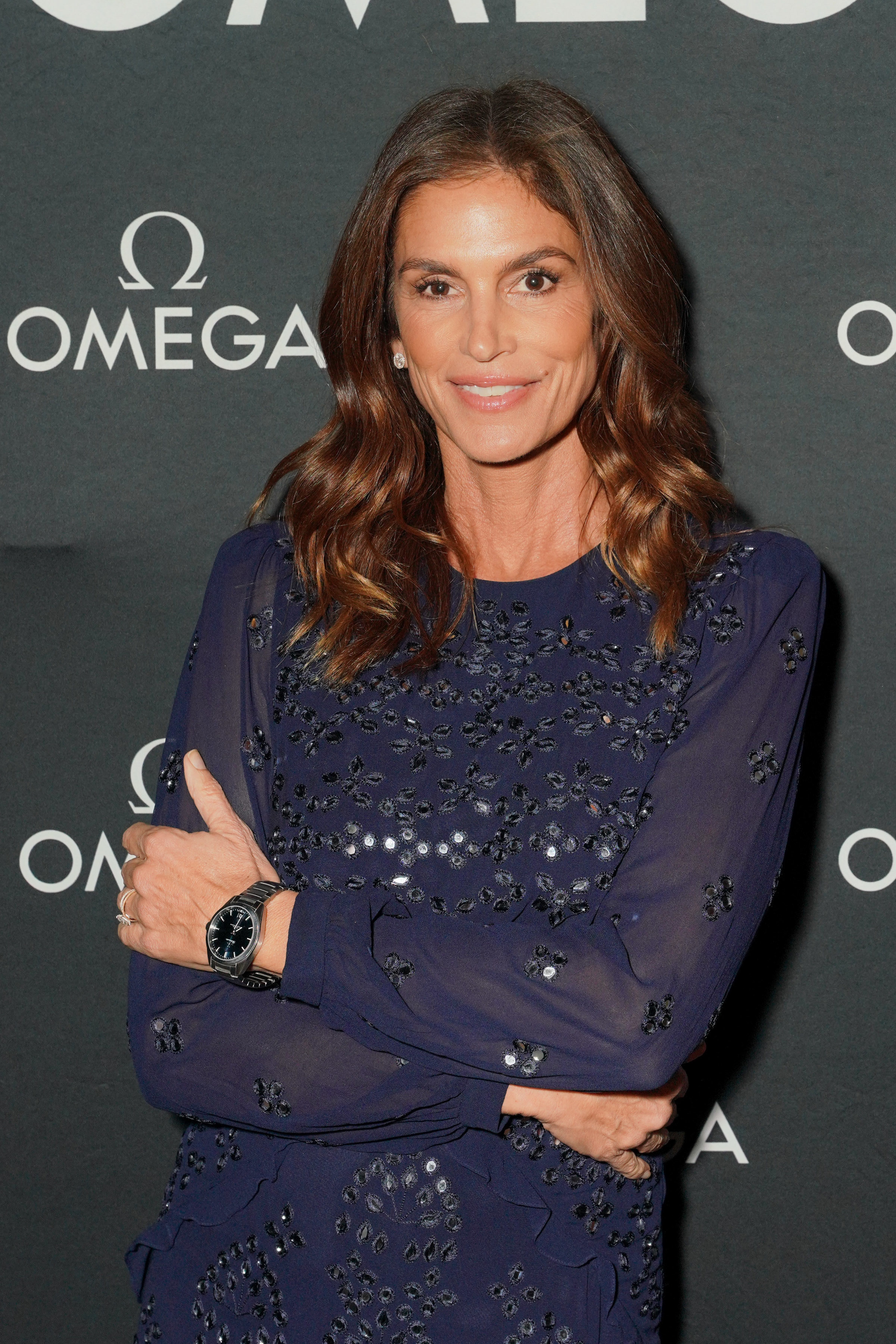 Cindy Crawford poses on the red carpet in a navy blue long-sleeve sheer dress