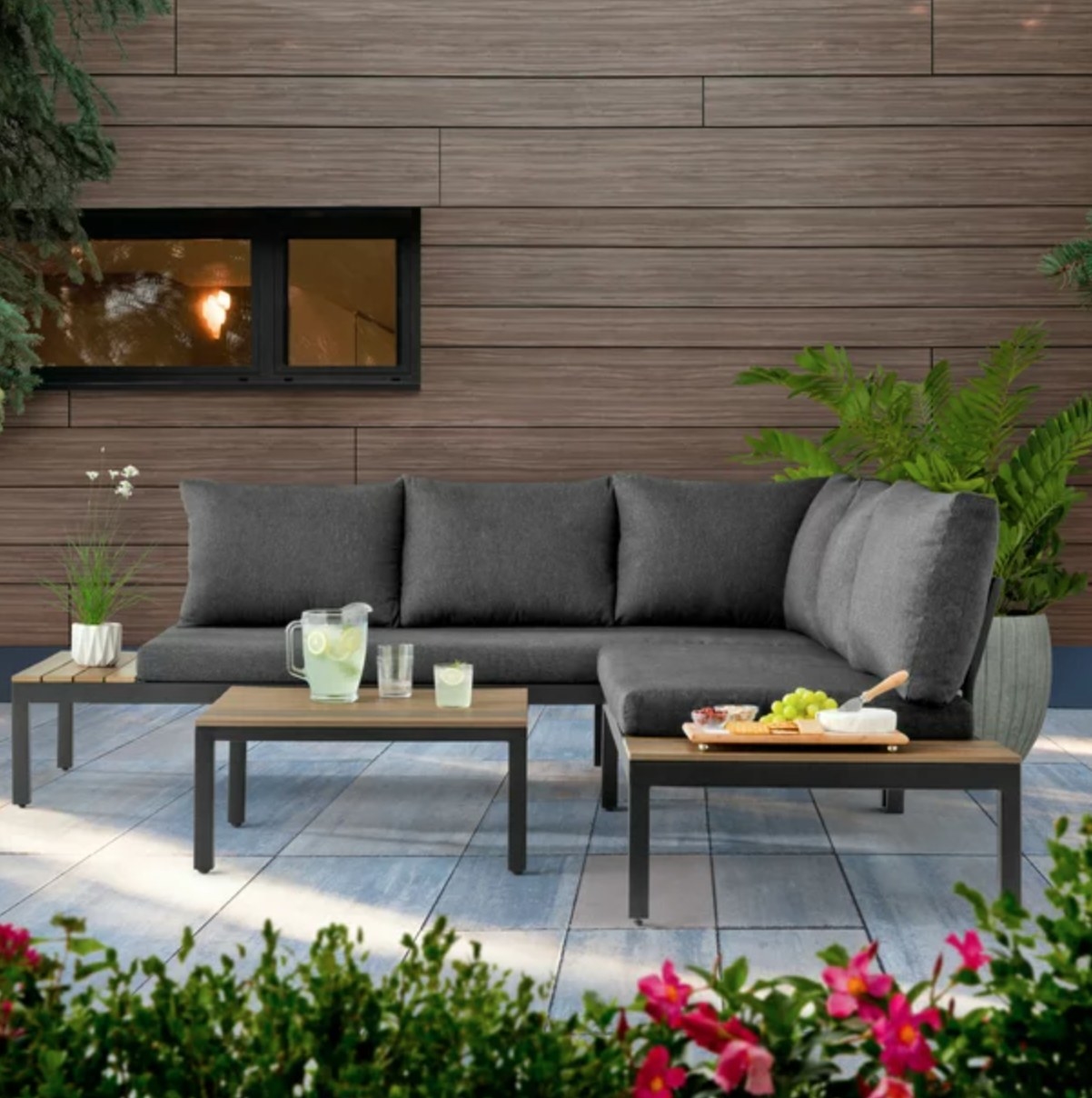 the grey sectional with attached light wood tables and a separate light wood coffee table in a decorated patio space
