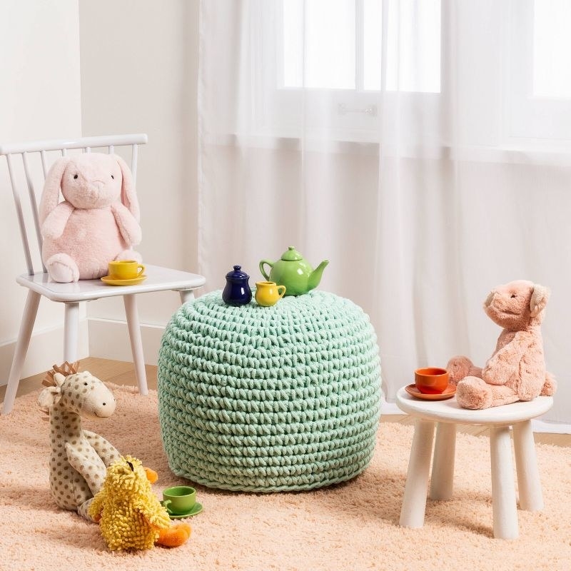a mint green woven ottoman surrounded by children&#x27;s chairs and toys